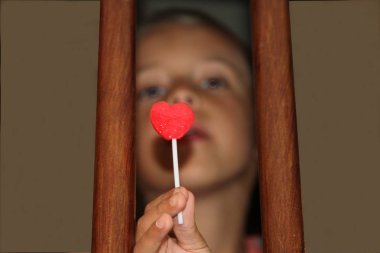 Çocuk merdiven direkleri arasında bir kalp şeklinde lolipop yalama