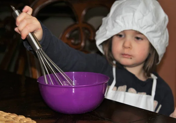 Young girl with cooks hat stirring food in a bowl