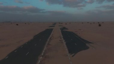 Dubai çölündeki asfalt yol kum fırtınası üstüne kum ile kaplı, gün batımında insansız hava aracı tarafından filme alındı..