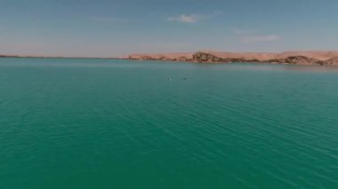 Ördekler mavi göl suyunun üzerinde uçar, onu drone kamerası takip eder.