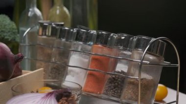 Mutfak masasında taze sebze ve baharat kavanozları var. Önünde kırmızı soğan doğranmış. Yavaş çekim