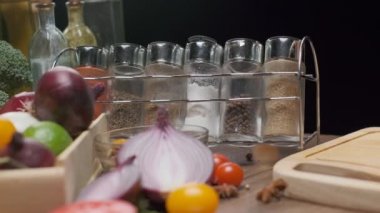 Mutfak masasında taze sebze ve baharat kavanozları var. Önünde kırmızı soğan doğranmış. Yavaş çekim