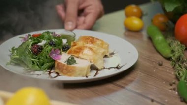 Tavuk rulosu ve yeşilliklerle servis edilen tabağın etrafında buharla.