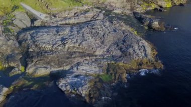 Kıyı kayalıkları ve tepedeki küçük şapel. Arka planda büyük yeşil bir dağ. İnsansız hava aracı
