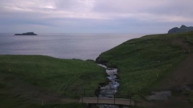 Faroe Adaları 'nın yeşil uçurumlarından denize küçük şelale düşüyor. İnsansız hava aracı.