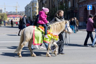 Krasnoyarsk, Rf - 9 Mayıs 2013: Zafer gün ikinci Dünya Savaşı kutlamaları sırasında Krasnoyarsk şehir cadde boyunca bir kız tarafından yönlendirilen akıllı beyaz bir midilli hediye üzerinde küçük bir kız biniyor. Krasnoyarsk Bölgesi. Rusya.