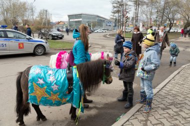 Krasnoyarsk, Rf - 9 Mayıs 2018: Çocuklar için binme, bir girlon gözetimi altında zarif midilli arka planını bir polis arabası zafer gün ikinci Dünya Savaşı kutlamaları sırasında baktı. Krasnoyarsk Bölgesi. Rusya.