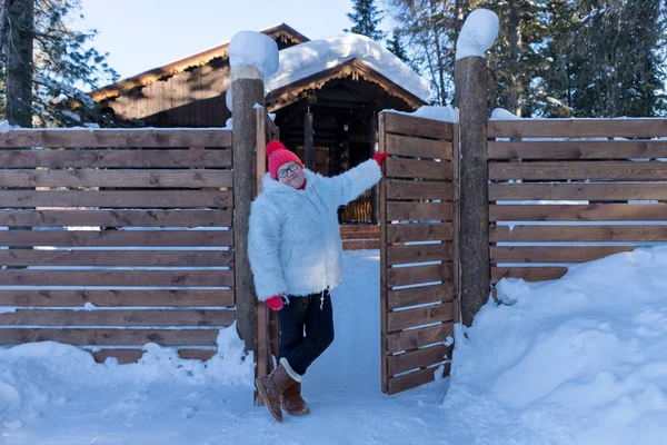 Geçidin yakınlarında orman snowdrifts arasında ahşap bir ev yakınındaki yaşlı bir kadın duruyor.