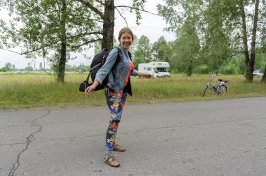 Bir yaz gününde ağaçlar arka planı yolda bir sırt çantası ile mutlu kız backpacker duruyor.
