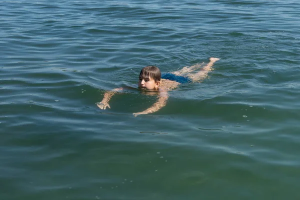 A boy of 11 years old is swimming in blue water.