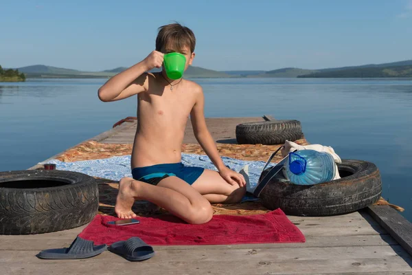 Årig Pojke Dricker Vatten Från Mugg Medan Sitter Träbrygga Mot — Stockfoto