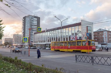 Krasnoyarsk, Krasnoyarsk Region / RF - October 29, 2018: A tram rides along Krasnoyarsk Worker's Avenue against the background of the White Owl Hotel. Building was built in 1968 as the hotel Vostok. clipart