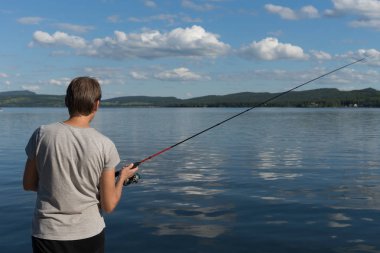 Kadın dağlık kıyı ve bulutlu gökyüzü karşı güzel bir mavi Gölü balık tutuyor. Doğal shot.