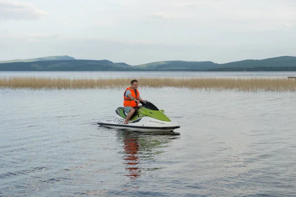 オレンジ色のライフ ジャケットの若い男夏の湖畔に水自転車に乗る — ストック写真