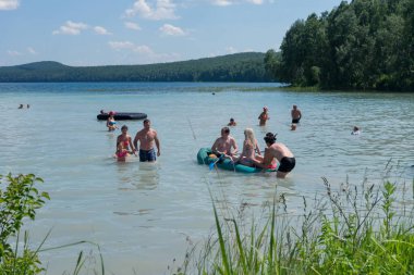 Ingol Lake, Sharypovo District, Krasnoyarsk bölgesi / Rf - 6 Temmuz 2014: insanlar bir şişme bot float, güneşlenmek ve güneşli yaz gününde yüzmeyi göle orman arka planı.