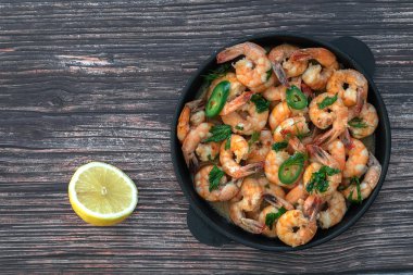 Masa üzerinde bir dökme demir tava krem sos Kızarmış karides, yarım limon yanında