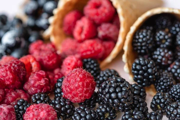 Raspberries, currants, blackberries closeup poured out of waffle cones, the focus is on raspberries — Stock Photo, Image