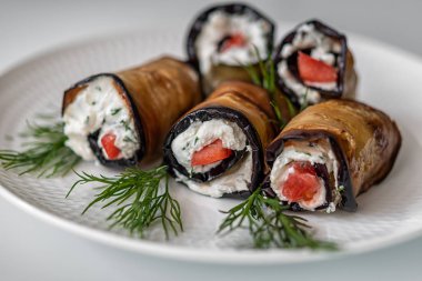 Beyaz bir arka plan üzerinde yakın çekim beyaz bir tabak üzerinde dereotu dalları ile süzme peynir ve domates ile Patlıcan rulo