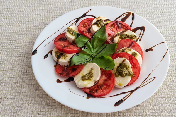 White plate of healthy classic delicious caprese salad with tomatoes and mozzarella cheese with basil leaves and strips of soy sauce. Italian concept. — Stock Photo, Image