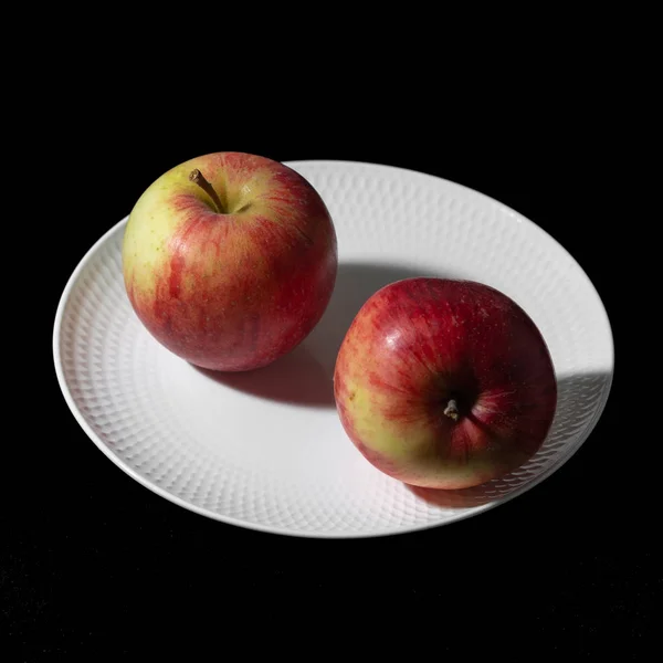 Two apples lie on a white plate on a black background close-up