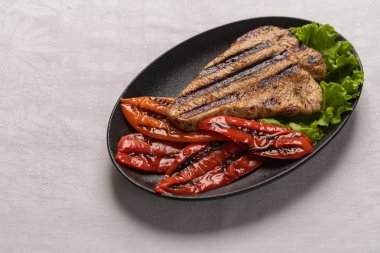 Pişmiş biber ve marul yaprakları ile ızgara Hindi göğüs biftek hafif keten arka plan üzerinde siyah bir tabakta. Yatay yönlendirme, kopyalama alanı