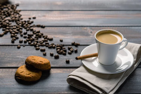 Xícara de café preto com canela e biscoitos em um guardanapo de linho em uma mesa de madeira escura. Grãos de café derramar para fora do saco na mesa . — Fotografia de Stock