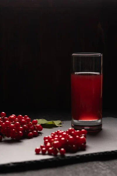 Red juice from viburnum in a glass on a black background. Near viburnum berries.Healthy food