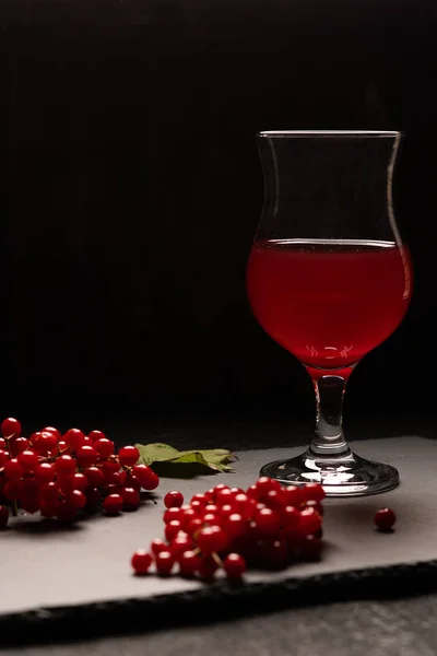 The red juice of viburnum with a stemmed glass on a black background. Near viburnum berries. Healthy food