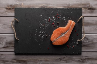 Çiğ somon bifteği. Kırmızı biber ve tuz ile koyu bir tahta üzerinde. Sağlıklı yiyecekler. Üst te. Ahşap arka plan