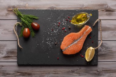 Çiğ somon bifteği. Karanlık bir tahtada. Domatesin, limonun yanında. Bir yağ da zeytinyağı. Sağlıklı yiyecekler. Üstte görüntü