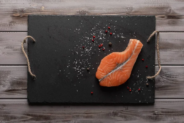 Çiğ somon bifteği. Kırmızı biber ve tuz ile koyu bir tahta üzerinde. Sağlıklı yiyecekler. Üst te. Ahşap arka plan