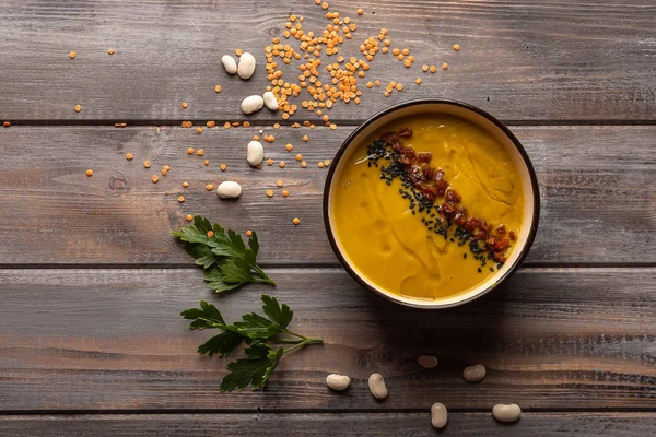 Ahşap bir arka plan üzerinde kırmızı biber ve siyah susam ile fasulye karışımı ile ev yapımı krema çorbası. Maydanoz yaprakları ve beyaz fasulye tabağına yakın. Üstte görüntü
