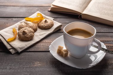 Bir fincan şekerli portakallı sıcak siyah kahve. Keten peçete ve açık bir kitap üzerinde Ccookies