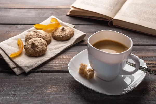 Bir fincan şekerli portakallı sıcak siyah kahve. Keten peçete ve açık bir kitap üzerinde Ccookies