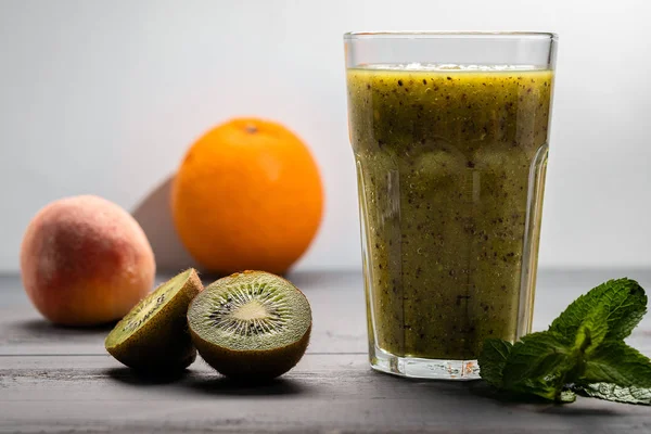 Kiwi smoothie on a light background. Next to the fruit and mint leaves. Healthy food for children and adults