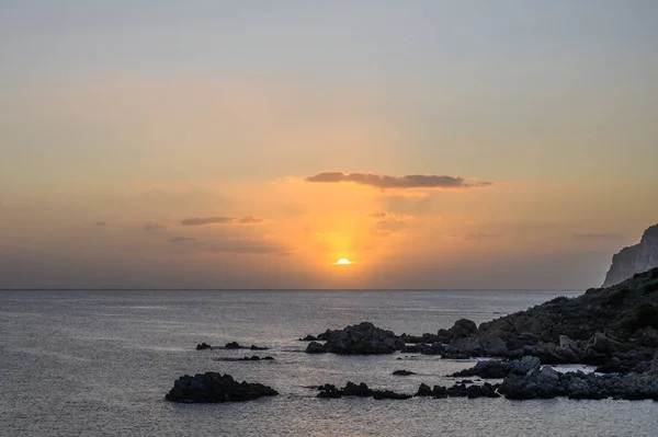 Amanecer sobre el mar. Los rayos del sol se reflejan en las nubes. En primer plano una costa rocosa — Foto de Stock