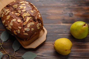 Tahta tepside zencefil ve kakule ile ev yapımı çikolatalı armut keki. Armutların ve yapraklı bir dalın yanında.