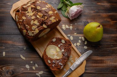 Tahta tepside zencefil ve kakule ile ev yapımı çikolatalı kek. Yarım armut ve kutunun yanında. Arka plandaki gül tomurcuğu