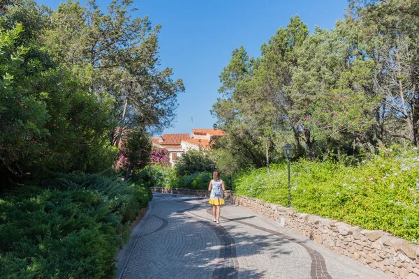 Woman view from behind walks along the path of a quiet Park in Porto Rotondo Sardinia on a clear day