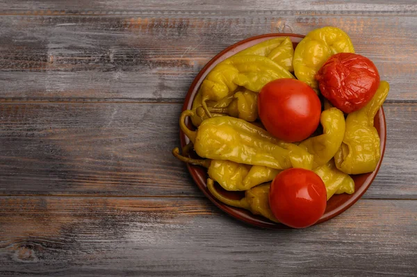 Pimentas conservadas em escabeche sortidas e tomates em uma chapa cerâmica em um contexto de madeira — Fotografia de Stock