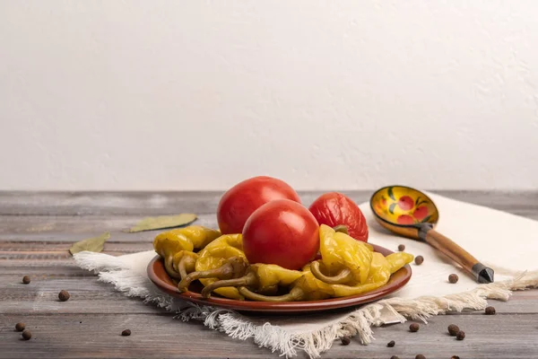 Домашний маринованный перец и помидоры на керамической тарелке на льняной салфетке. Рядом с традиционной русской деревянной ложкой — стоковое фото