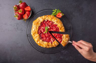 Kadınların elinde, koyu arkaplanda çilek, nane ve badem içeren bir dilim pasta bulunan bir spatula var. Boşluğu kopyala