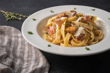 Mantarlı makarna, pastırma, beyaz tabakta parmesan peyniri ve siyah ahşap kaplama peçeteli makarna.