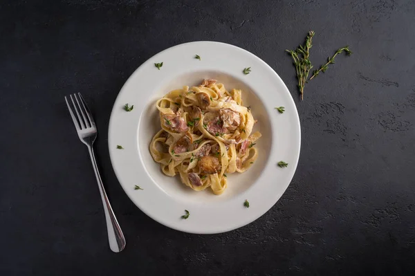 Fettuccine di pasta con funghi, pancetta e parmigiano in piatto bianco su fondo di grafite scura vista dall'alto — Foto Stock