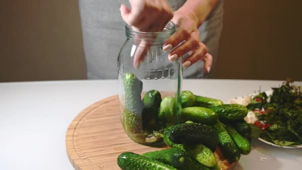 Жінка кладе спеції і свіжі огірки в скляну банку, готуючись до консервування — стокове відео