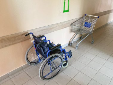 Hastane koridorunda tekerlekli sandalye ve boş market arabası, kopyalama alanı.