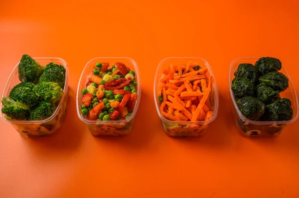 Frozen vegetables carrot, broccoli, spinach, green pods beans in plastic trays on an orange background, close up — Stock Photo, Image