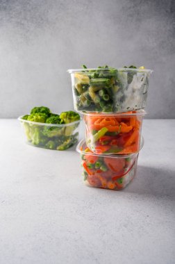 Donmuş sebzeler havuç, brokoli, ıspanak, yeşil tohumlar plastik tepsilerde hafif arka planda, kapat.