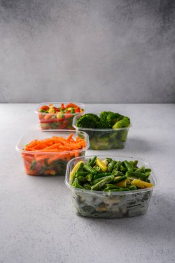 Donmuş sebzeler havuç, brokoli, ıspanak, yeşil kabuklu yeşil fasulyeler gri arka planda plastik tepsilerde, kapat.