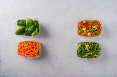 Donmuş sebzeler havuç, brokoli, yeşil tohumlar plastik tepsilerde hafif arka plan, üst manzara